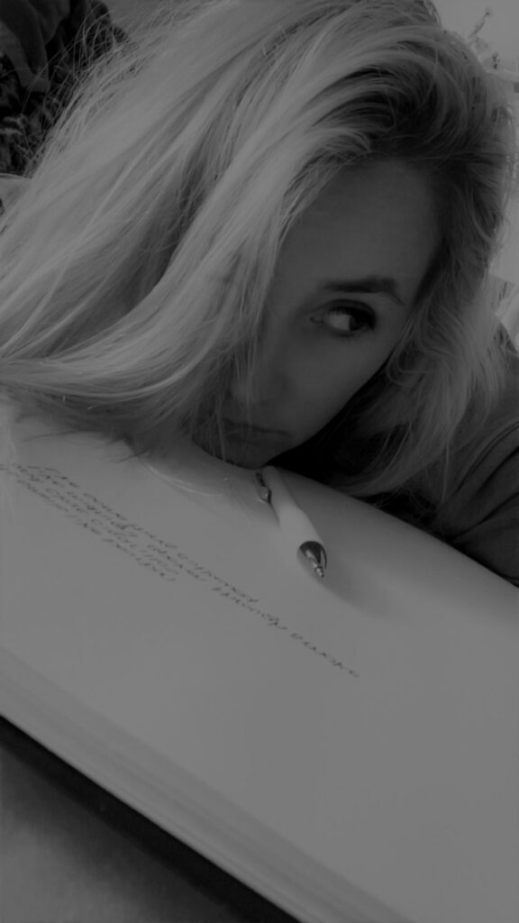 Nikyla Maria in black and white, her cheek resting on an open notebook, one eye looking up.