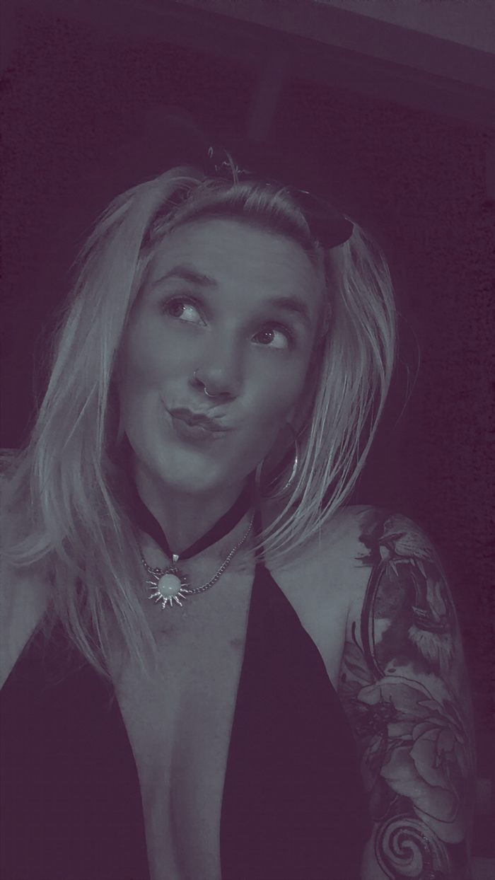 Nikyla pulling a duck face, eyes sliding sideways, in purple-tinted light.