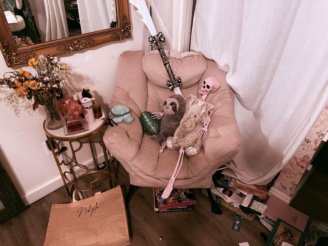 A pink armchair holding a pink skeleton, a stuffed sloth, a dragon egg and a toy sword.