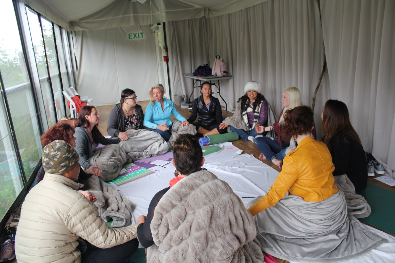 A circle of women sitting together on blankets inside a tent.