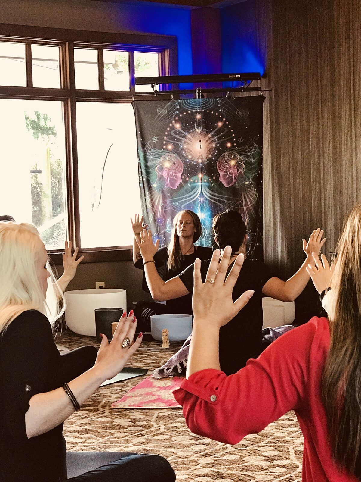 A retreat circle with hands raised in front of a tapestry, singing bowls on the floor.