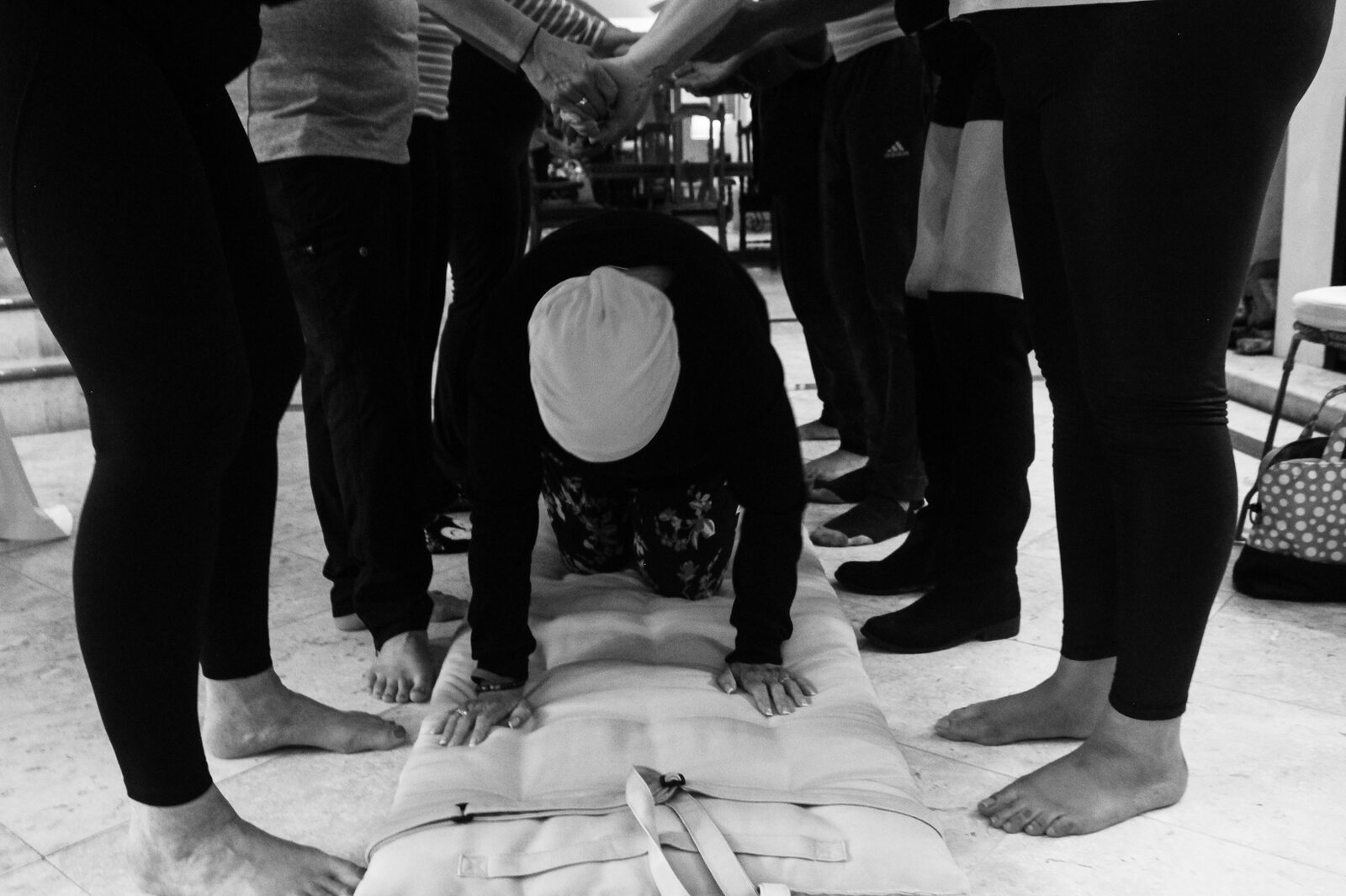 Black-and-white photograph of a woman crawling through a tunnel of legs on a mat during a ritual.