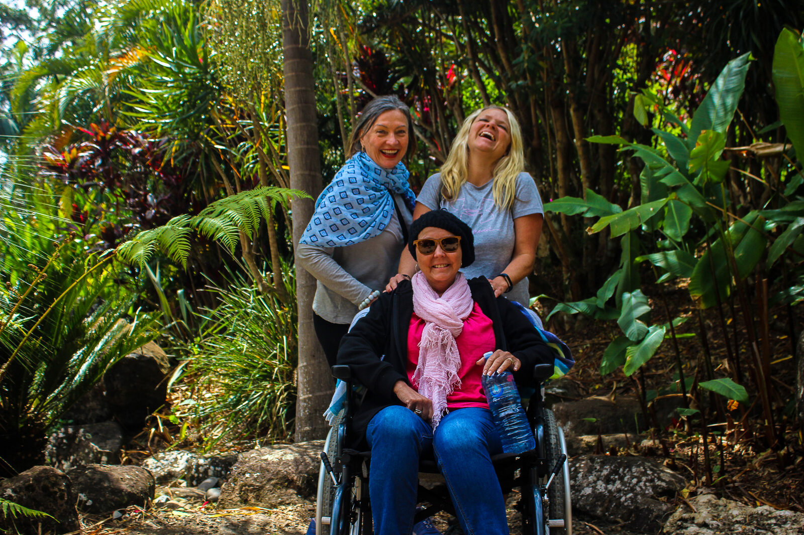 Three women laughing together in a tropical garden.