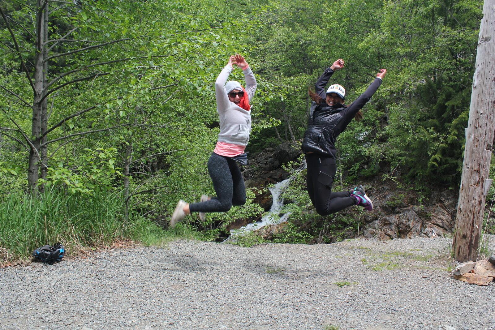 Two women leaping in the air on a forest trail.