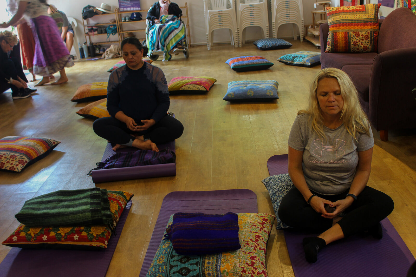 Women sitting cross-legged on cushions in a bright meditation room.
